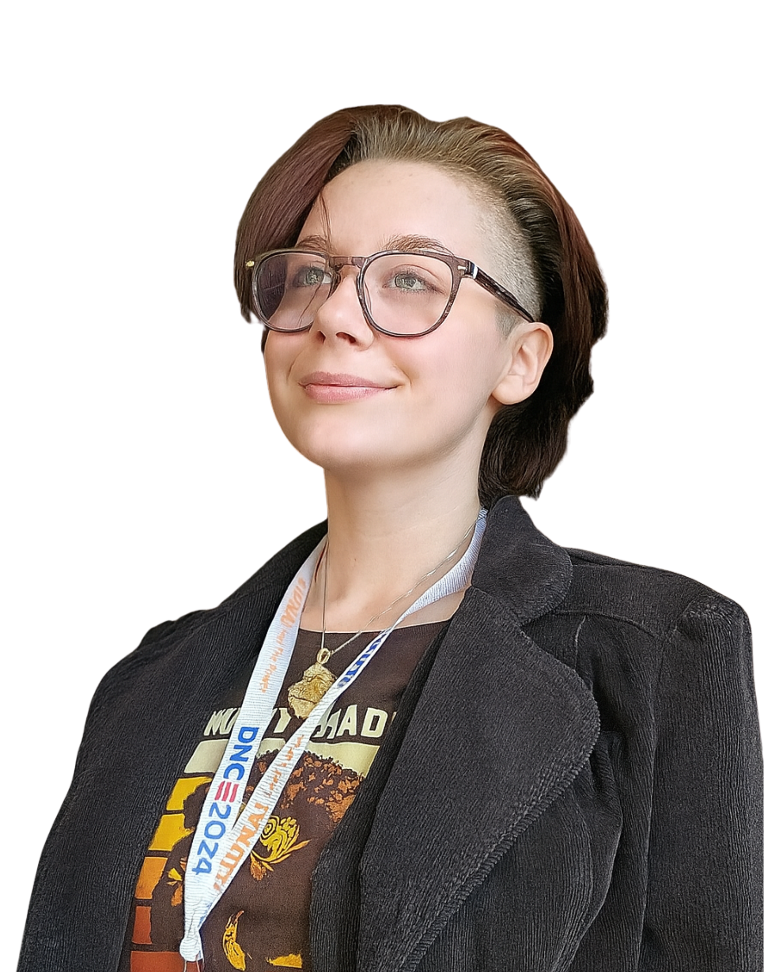 A woman with a short hairstyle, glasses, and a badge around her neck poses confidently with a slight smile, wearing a black blazer and a graphic t-shirt.