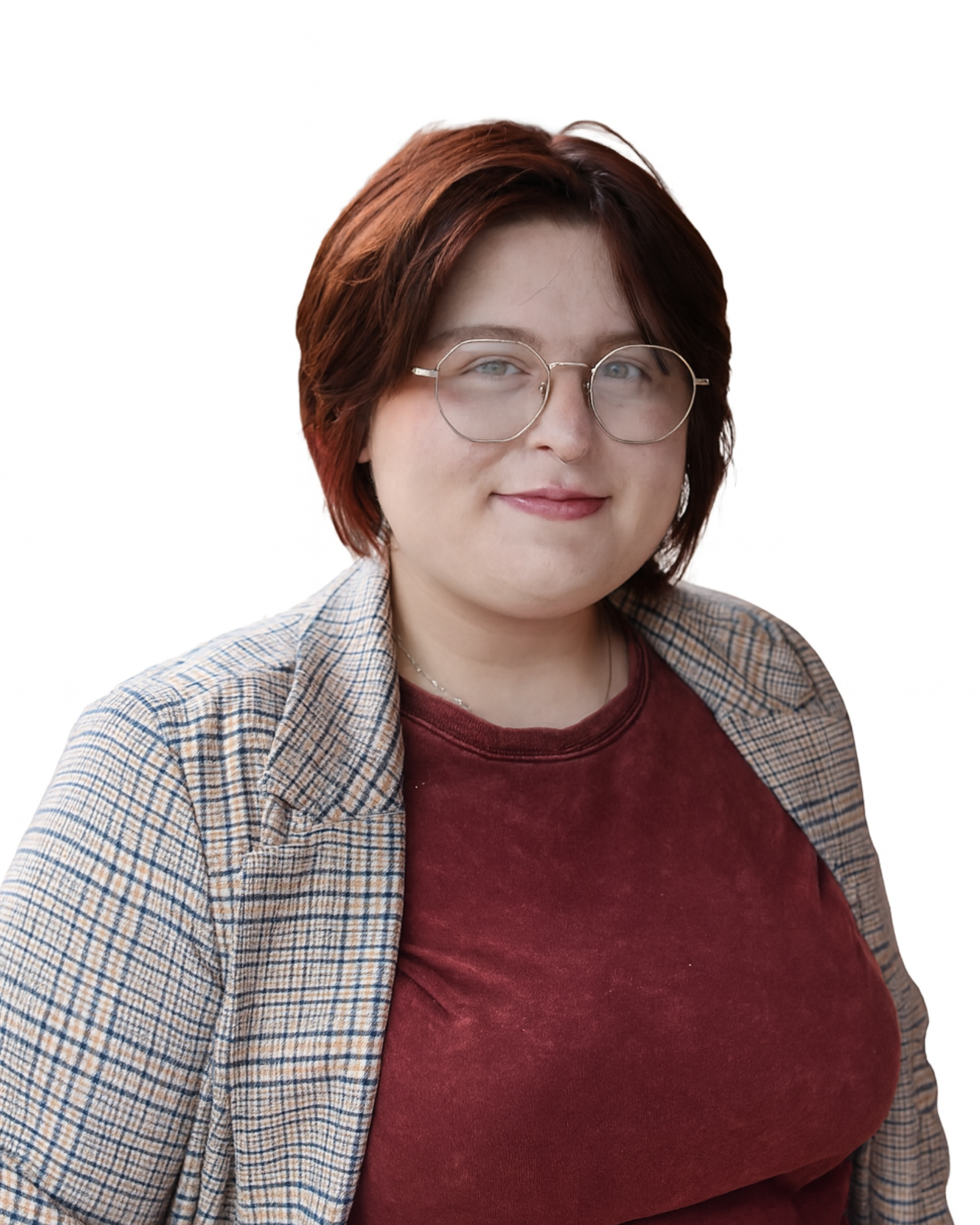 Close-up of a young woman with short red hair, round glasses, a nose ring, wearing a burgundy shirt and a plaid blazer, smiling.
